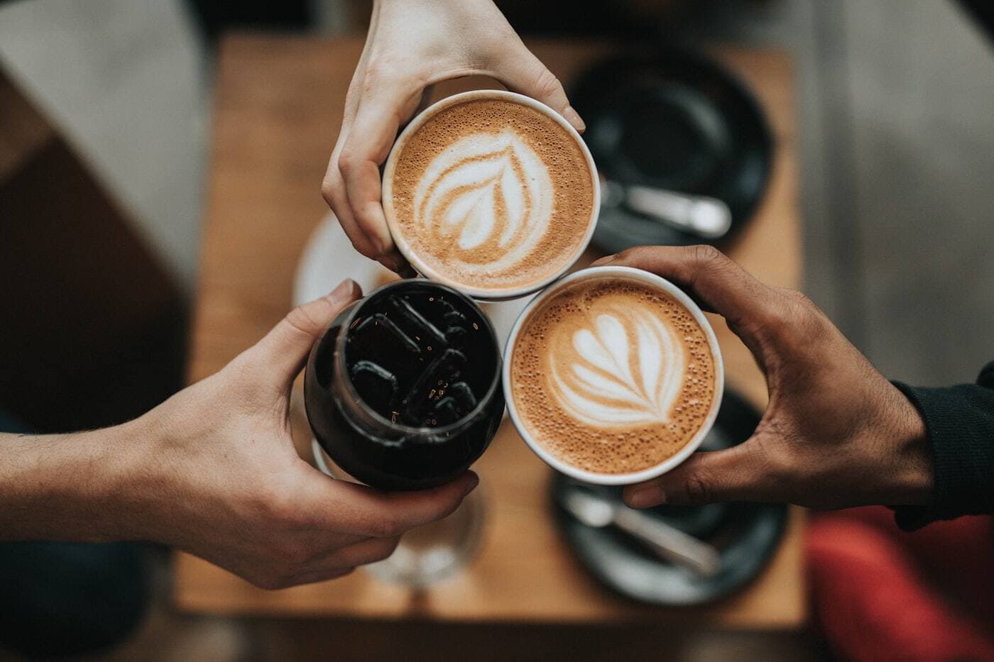 Three friends touching coffee cups together across a café table